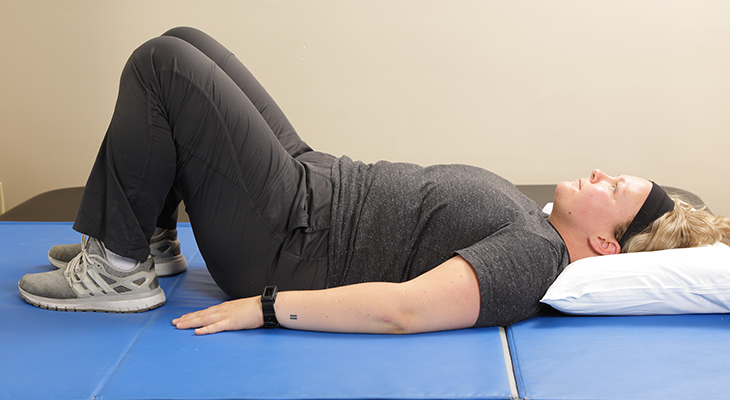 A patient demonstrates the first part of the bridges back pain exercise.