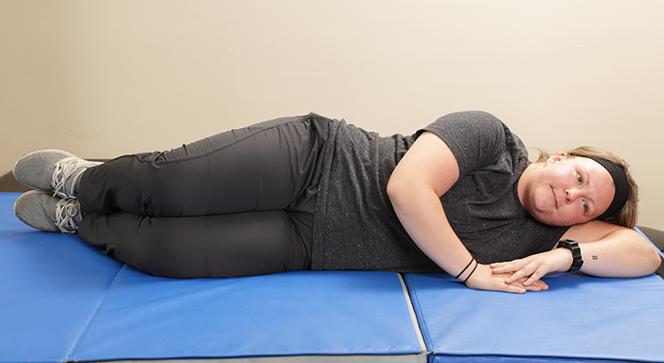 A patient demonstrates the first part of the clamshells back pain exercise