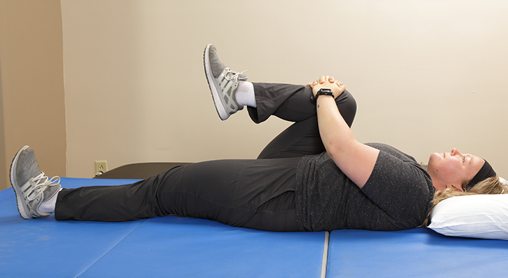 A patient demonstrates the single knee to chest stretch back pain exercise.